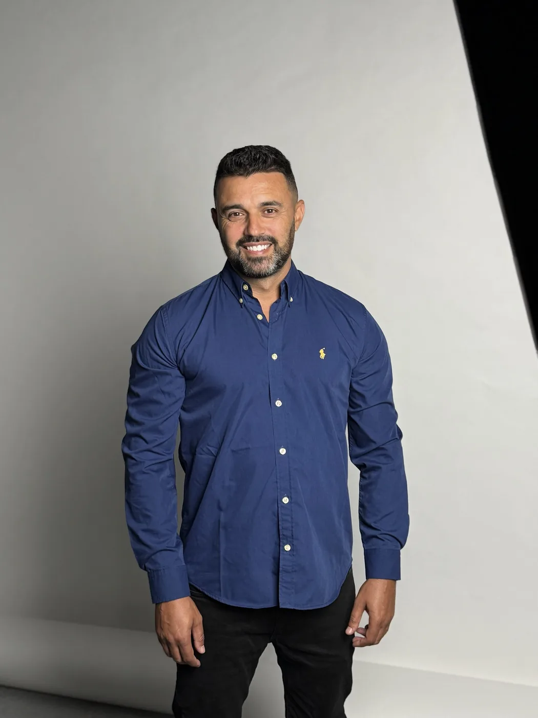 Retrato de André Braga, de camisa azul, sobre fundo claro de estúdio.